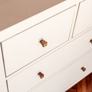 May include: White dresser with six drawers and wooden knobs. The dresser has a light wood finish and is made of solid wood.