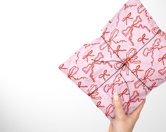 May include: Pink gift wrap with a red and white pattern of bows. The wrap is tied with black string.