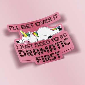 May include: A pink sticker with the text "I'll get over it. I just need to be dramatic first." A white unicorn with a rainbow mane and tail is lying down on the sticker. The sticker has a shadow.