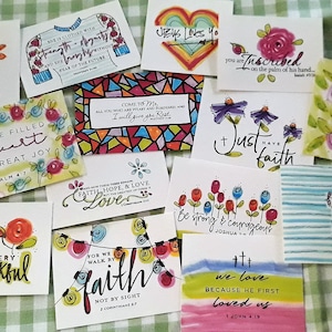 May include: A collection of 12 colorful cards with inspirational quotes and bible verses. The cards feature hand-drawn illustrations of flowers, hearts, and other designs. The cards are perfect for adding a touch of faith and inspiration to your home or office.
