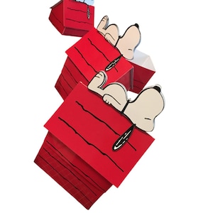 Puede incluir: Figuras tridimensionales de casetas de Snoopy en rojo con líneas negras y figuras de Snoopy. Snoopy está acostado encima de las casetas. El fondo es blanco.