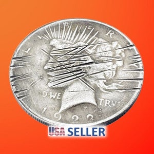 May include: A silver Peace Dollar coin with a design of a woman's head with rays of light behind it. The coin has the year 1922 inscribed on it. The coin is scratched and worn.