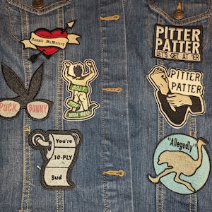 May include: A denim jacket with various embroidered patches, including a heart with the text "Donnie McMurray", a toilet paper roll with the text "You're 10-PLY Bud", a bunny with the text "Puck Bunny", a figure with the text "MODA WATO", and two patches with the text "PITTER PATTER".