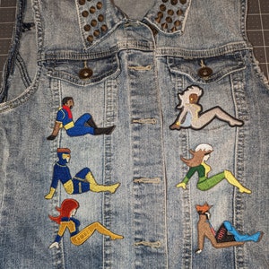 May include: A denim vest with a studded collar and embroidered patches of various characters from the X-Men comic book series. The patches are in a variety of colors, including blue, yellow, red, green, and black.
