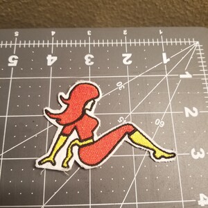 May include: Red and yellow embroidered iron-on patch of a woman sitting with her legs crossed.