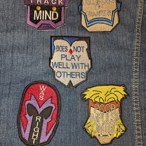 Peut inclure: Cinq patchs brod&eacute;s thermocollants avec des dictons diff&eacute;rents. Les patchs sont sur un fond en jean bleu. Les patchs sont violets, bleus, rouges, blancs et jaunes. Les dictons sur les patchs sont "One Track Mind", "Delusions of Grandeur", "Does Not Play Well With Others", "Was Right", and "Poor Impulse Control".