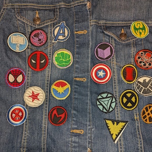 May include: A blue denim jacket with various embroidered patches featuring characters and symbols from the Marvel Cinematic Universe. The patches include Captain America, Iron Man, Thor, Hulk, Black Widow, Hawkeye, Spider-Man, and more.