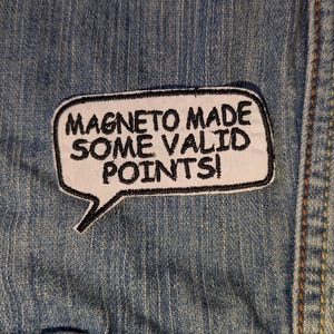May include: A white patch with black text that reads "MAGNETO MADE SOME VALID POINTS!" in a speech bubble shape. The patch is sewn onto a blue denim fabric.