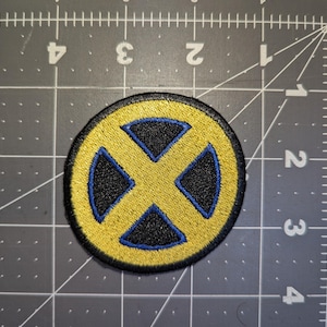 May include: Embroidered patch featuring the iconic yellow and blue X-Men logo. The circular patch has a black background with a yellow "X" design and blue accents. The patch is likely for clothing or accessories.