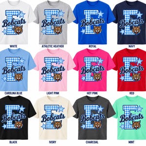 Puede incluir: Una colección de doce camisetas de manga corta en varios colores, incluyendo blanco, gris, azul, rosa, rojo, negro, marfil y menta. Cada camiseta presenta una letra E grande con un patrón de cuadros azules, la palabra Bobcats y un lince.