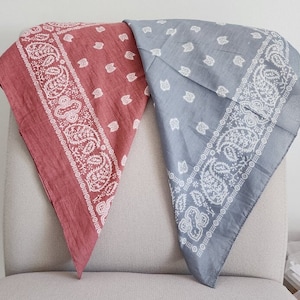 May include: Two cotton bandanas, one red and one gray, with a white paisley pattern. The bandanas are folded and laid out on a gray fabric surface.