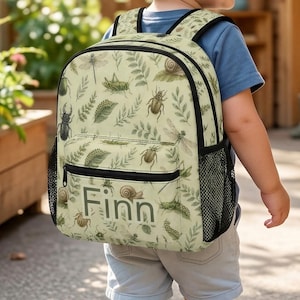 May include: A light green backpack featuring a repeating pattern of various insects, snails, and fern leaves. The front pocket displays the name Finn in dark lettering. The bag includes black zippers, adjustable shoulder straps, and side mesh pockets.