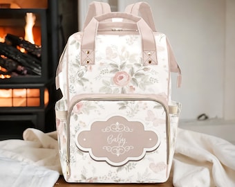 May include: A floral print diaper bag with a pink and gold design. The bag has a large pocket on the front with a gold-colored label that says "Baby".