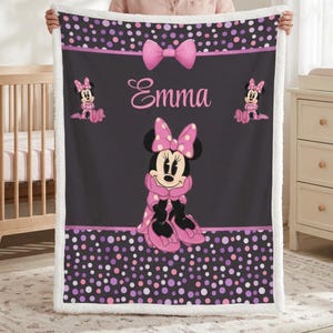 May include: A rectangular fleece blanket featuring a dark gray center with a large Minnie Mouse graphic, the name Emma in pink script, and a pink bow. The top and bottom borders have a black background with pink and purple polka dots.