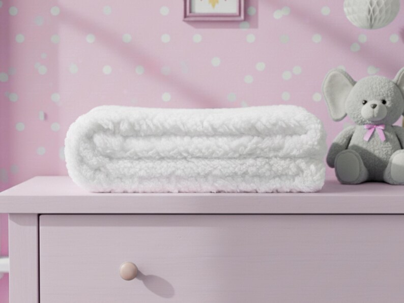 May include: A folded white blanket with a thick, plush, sherpa-like texture. The blanket is rectangular in shape and features a dense, curly pile surface that appears soft and warm. It is positioned horizontally, showcasing its layered, folded structure.