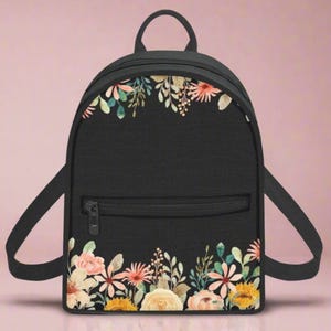 May include: A black backpack with a floral print. The flowers are in shades of pink, yellow, and green. The backpack has a zipped pocket on the front.