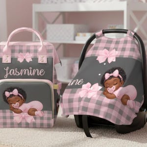 May include: A pink and grey checked diaper bag and car seat cover set. The diaper bag has the name "Jasmine" embroidered on it. Both items feature illustrations of a baby girl with a bow and pacifier.