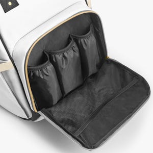 Peut inclure: Sac &agrave; langer blanc avec plusieurs poches int&eacute;rieures. Le sac a une fermeture &eacute;clair dor&eacute;e et des poches int&eacute;rieures noires. Le sac a une poche en filet et trois petites poches. Le sac a une sangle beige et des accents noirs.