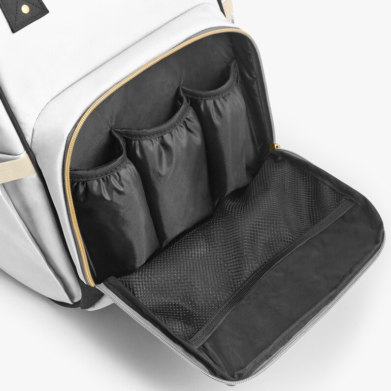 Peut inclure: Sac &agrave; langer blanc avec plusieurs poches int&eacute;rieures. Le sac a une fermeture &eacute;clair dor&eacute;e et des poches int&eacute;rieures noires. Le sac a une poche en filet et trois petites poches. Le sac a une sangle beige et des accents noirs.