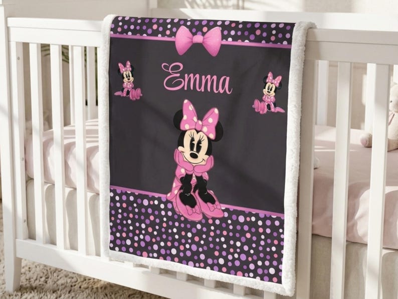 May include: A black and pink fleece blanket featuring a central illustration of Minnie Mouse, the name Emma in pink script, a pink bow at the top, and smaller Minnie Mouse figures on the sides. The border has a pattern of pink and purple polka dots.