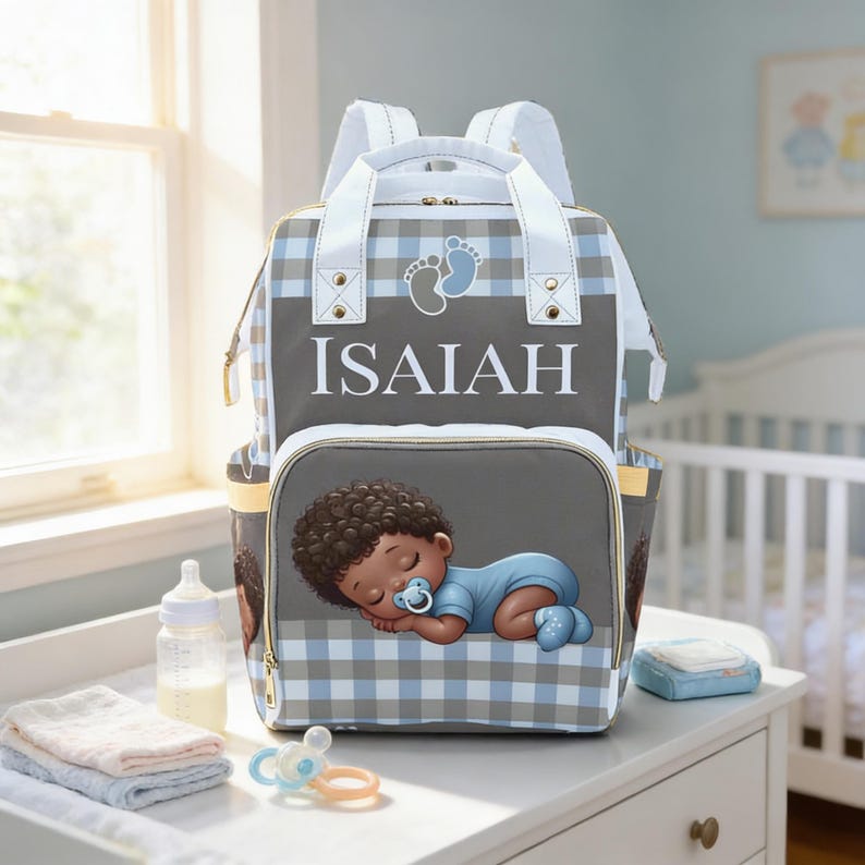 A gray and white backpack with a baby boy sleeping on it, placed on a white dresser next to a bottle and other baby supplies.