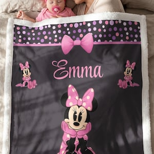 May include: A soft, plush fleece blanket featuring a black background with a large Minnie Mouse character in a pink polka-dot dress and bow. The blanket includes a pink bow graphic, a polka-dot border, and the name Emma printed in pink script.