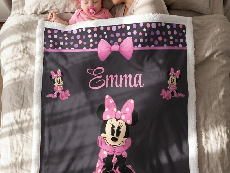 May include: A soft, plush fleece blanket featuring a black background with a large Minnie Mouse character in a pink polka-dot dress and bow. The blanket includes a pink bow graphic, a polka-dot border, and the name Emma printed in pink script.