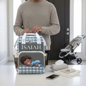 A man is holding a backpack with a baby image on it, standing in a room with a baby stroller and other items on the table.