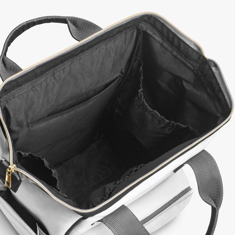 Peut inclure: Vue ouverte d'un sac fourre-tout gris et blanc avec un int&eacute;rieur noir. Le sac est dot&eacute; d'une poign&eacute;e sup&eacute;rieure et de bretelles. Une fermeture &eacute;clair dor&eacute;e longe le haut. L'int&eacute;rieur comporte plusieurs poches.