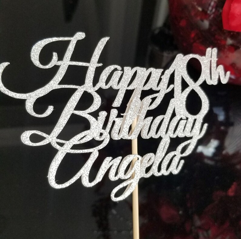 Pode incluir: Topper de bolo de glitter prata com o texto "Happy 18th Birthday Angela" em fonte cursiva.
