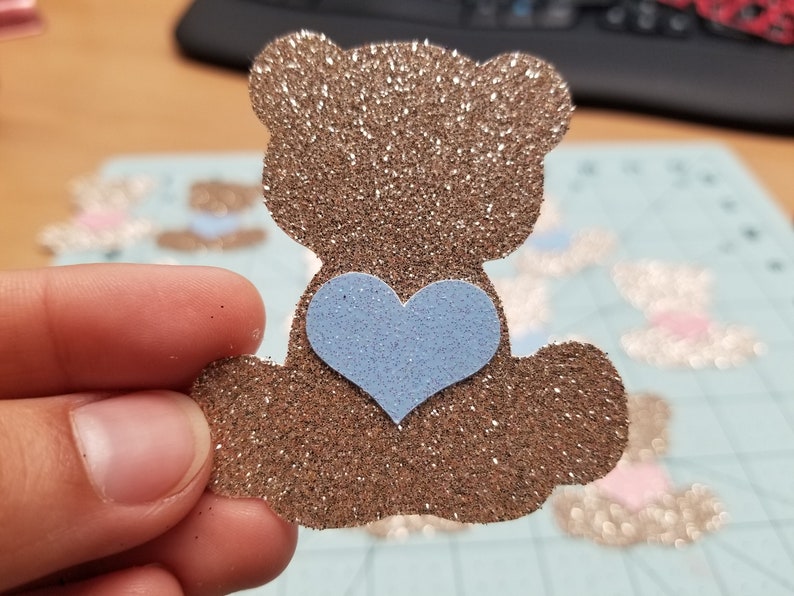 May include: A brown glitter teddy bear with a light blue glitter heart on its chest.