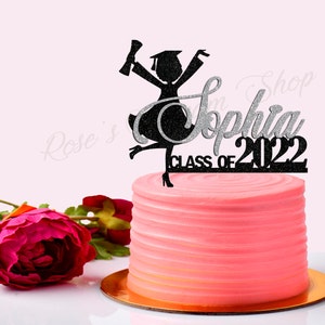 May include: Black and silver glitter graduation cake topper with a silhouette of a female graduate holding a diploma and the text "Sophia Class of 2022".