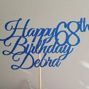 Pode incluir: Topper para bolo de glitter azul com o texto "Happy 68th Birthday Debra".