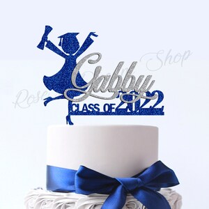 May include: Blue and silver glitter graduation cake topper with the name "Gabby" and the text "Class of 2022".