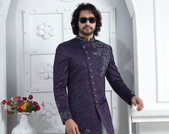 Op de afbeelding: Een lange, paarse kurta met een patroon, een witte knoopsluiting en een witte broek. De kurta heeft een mandarijnkraag en is geborduurd met zilverdraad. De man draagt witte schoenen.