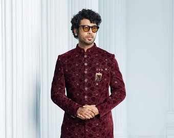 May include: A maroon velvet long-sleeved jacket with a floral pattern and gold buttons. The jacket has a mandarin collar and a pocket on the chest with a gold chain detail.