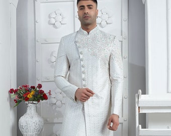 May include: A white long-sleeved button-up jacket with a subtle pattern and a single button closure on the left side. The jacket is worn over white pants and white shoes.
