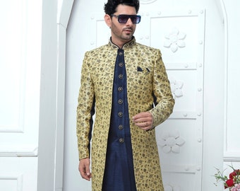 Puede incluir: Un hombre con una chaqueta larga de color dorado con estampado sobre una kurta azul marino y pantalones a juego. Lleva gafas de sol y zapatos dorados.