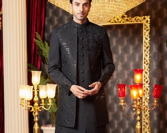 Könnte beinhalten: Eine schwarze, bestickte Herren-Kurta mit Mandarinkragen und Knopfleiste. Die Kurta wird mit einer schwarzen Hose und schwarzen Schuhen kombiniert. Das Model steht vor einem goldgerahmten Spiegel und einem goldenen Kandelaber mit roten Glasschirmen.