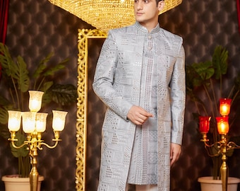 May include: A silver gray patterned kurta with a mandarin collar and a white bottom. The kurta is embroidered with silver sequins and has a long, flowing design. The model is wearing white pants and black shoes.