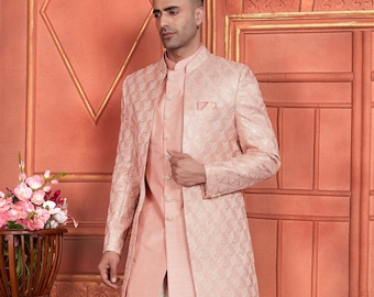 Puede incluir: Una chaqueta larga de color rosa y dorado con estampado, con una kurta rosa a juego y pantalones blancos. El atuendo lo lleva una persona de pie frente a una pared de color melocotón con un marco de puerta decorativo. El texto "D.NO. 2748" es visible en la esquina inferior derecha de la imagen.
