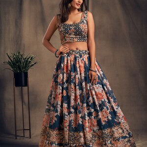 May include: A blue crop top with floral embroidery and a matching floral print skirt. The skirt has a gold embroidered border.