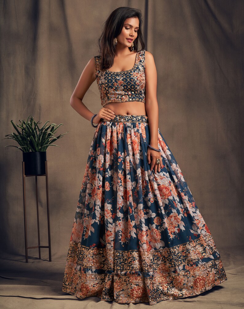 May include: A blue crop top with floral embroidery and a matching floral print skirt. The skirt has a gold embroidered border.