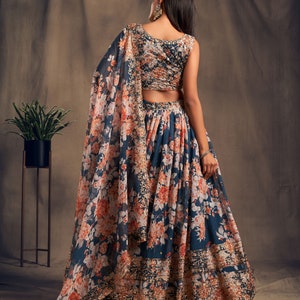 May include: A teal blue and peach floral print lehenga with a matching sleeveless blouse. The lehenga has a gold embroidered border and the blouse has a gold embroidered neckline.