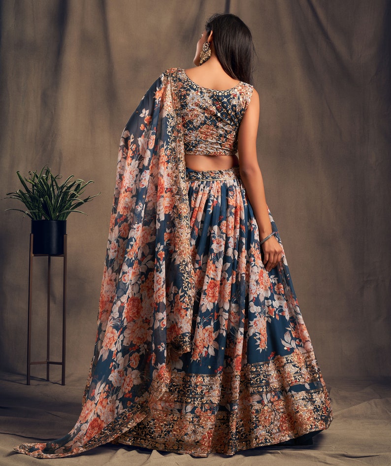 May include: A teal blue and peach floral print lehenga with a matching sleeveless blouse. The lehenga has a gold embroidered border and the blouse has a gold embroidered neckline.