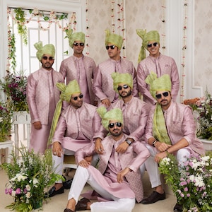 May include: A group of men wearing pink and green traditional Indian clothing. They are all wearing sunglasses and green turbans. The men are standing in a room with white walls and floral decorations.