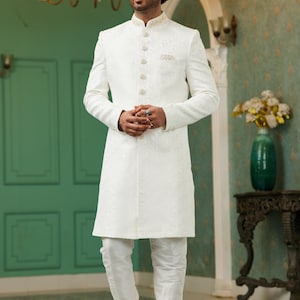 Puede incluir: Una kurta blanca de manga larga con cierre de botones y un dise&ntilde;o bordado blanco. La kurta se combina con pantalones blancos y zapatos de cuero negro.