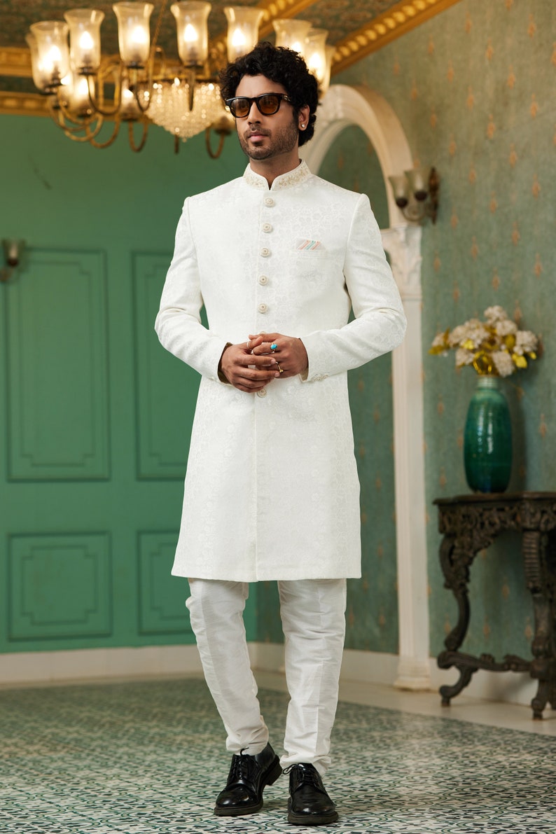 Puede incluir: Una kurta blanca de manga larga con cierre de botones y un dise&ntilde;o bordado blanco. La kurta se combina con pantalones blancos y zapatos de cuero negro.