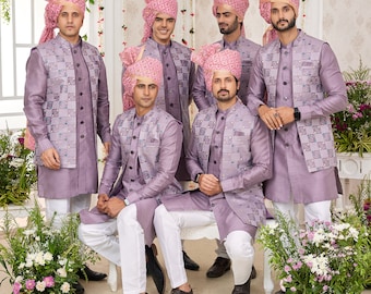 May include: A group of six people wearing matching formal attire. They are dressed in lavender-colored jackets with a geometric pattern, white pants, and matching turbans. The setting appears to be a formal event or wedding.