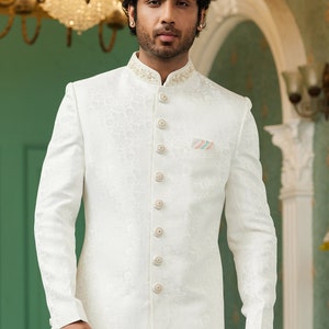 Puede incluir: Una camisa blanca de manga larga con botones, con un estampado floral y un bolsillo en el lado izquierdo. La camisa tiene un cuello mandar&iacute;n y una fila de botones en la parte delantera.